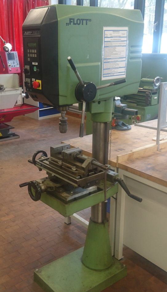 Bohrmaschine Flott P30 Das Bild zeigt eine Standbohrmaschine mit Kreuztisch und Schraubstock. Die Bohrmaschine steht in einer mechanischen Werkstatt.