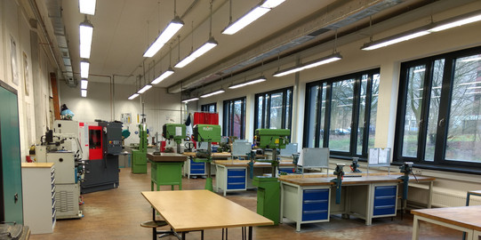 Das Bild zeigt eine totale der Ausbildungswerkstatt Metall der TU Dortmund. Zu sehen sind die Werkbänke der Auszubildenden, zwei Standbohrmaschinen und eine Drehmaschine.