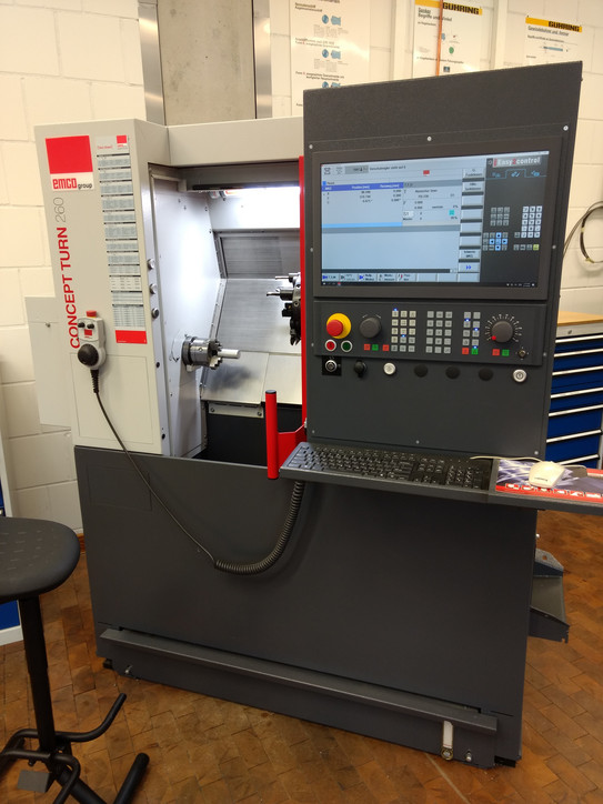 CNC-Drehmaschine Emco Concept Turn 260 Das Bild zeigt eine betriebsbereite CNC-Drehmaschine der Firma Emco. Die Schutztür ist geöffnet und die Innenraumbeleuchtung ist eingeschaltet.