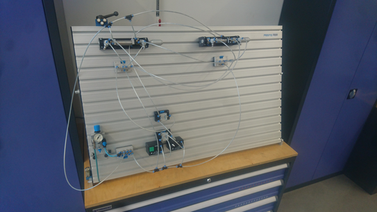 Pneumatikboard Das Bild zeigt eine T-Nutenplatte auf der einige Pneumatikkomponeten zu einer Schaltung mit zwei Pneumatikzylindern aufgebaut sind.